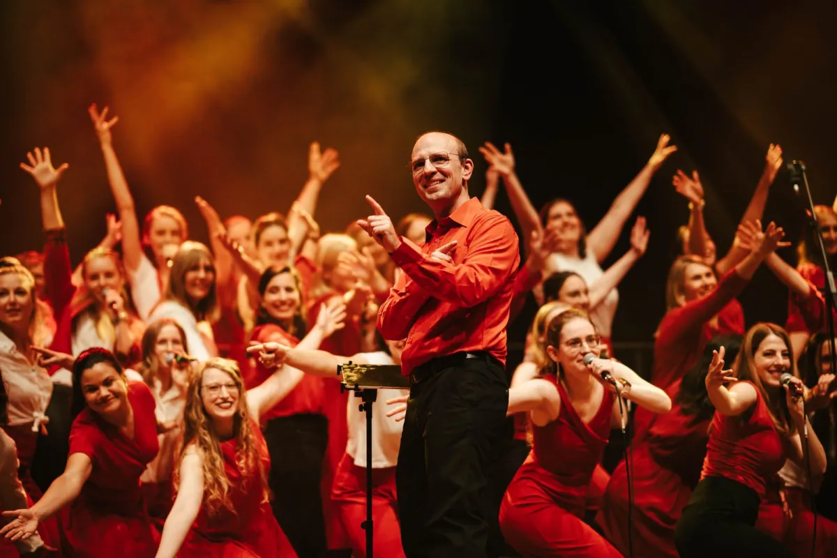 Choriosity: Chorleiter und Chor in Rot mit erhobenen Armen